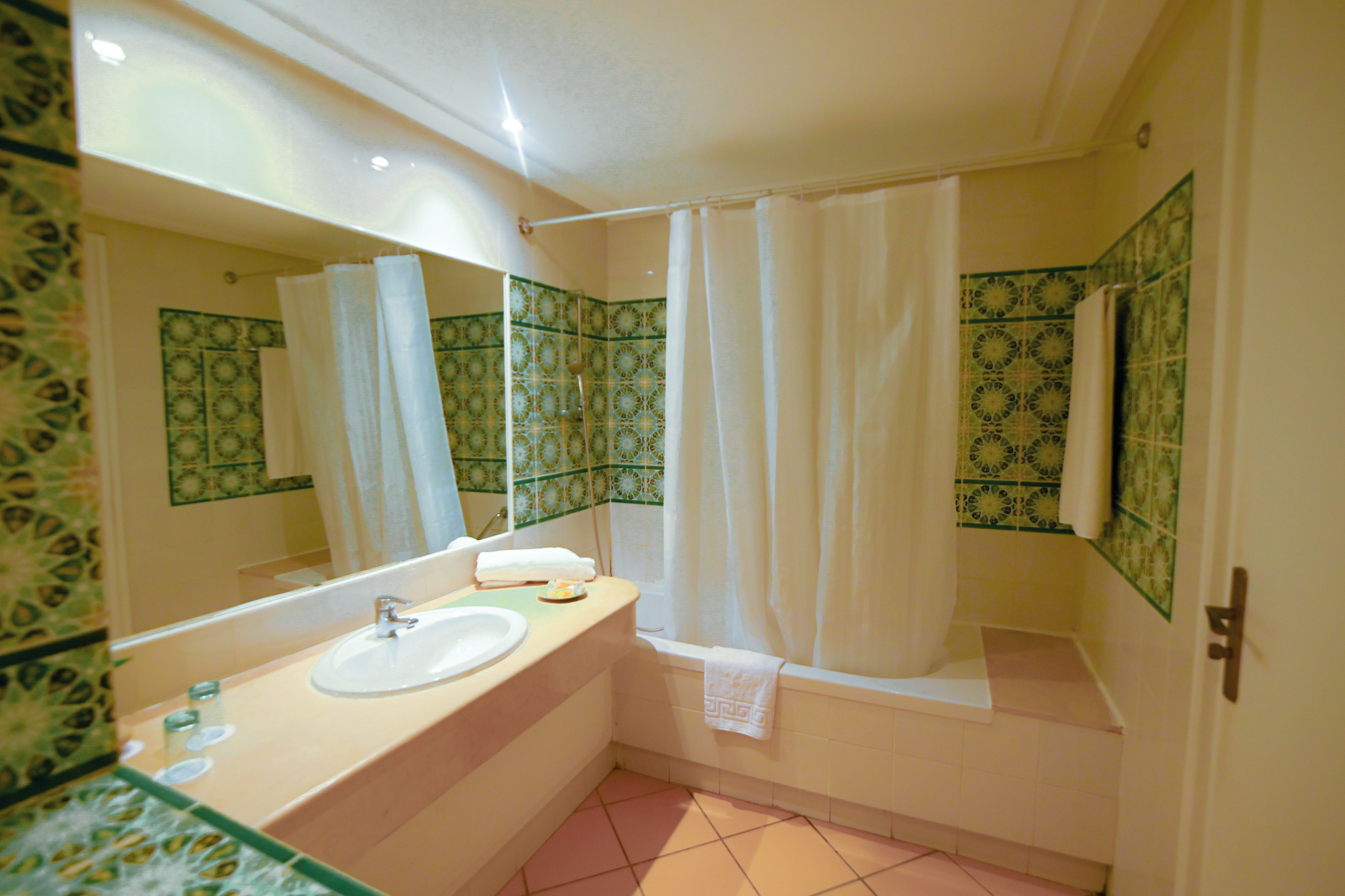 Un baño con lavamanos, espejo, ducha y azulejos estampados.