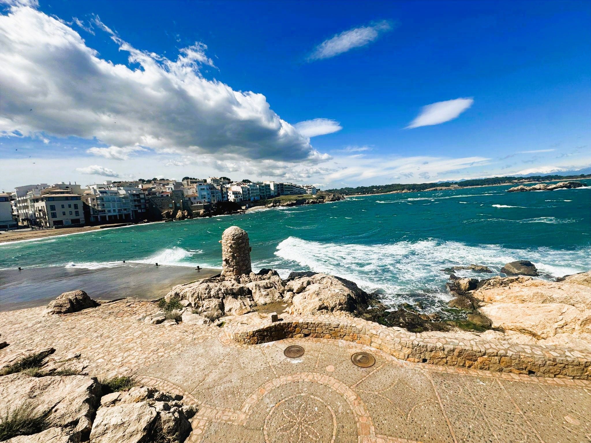 A coastal view with a stone pathway leading to a rocky outcrop overlooking the sea.