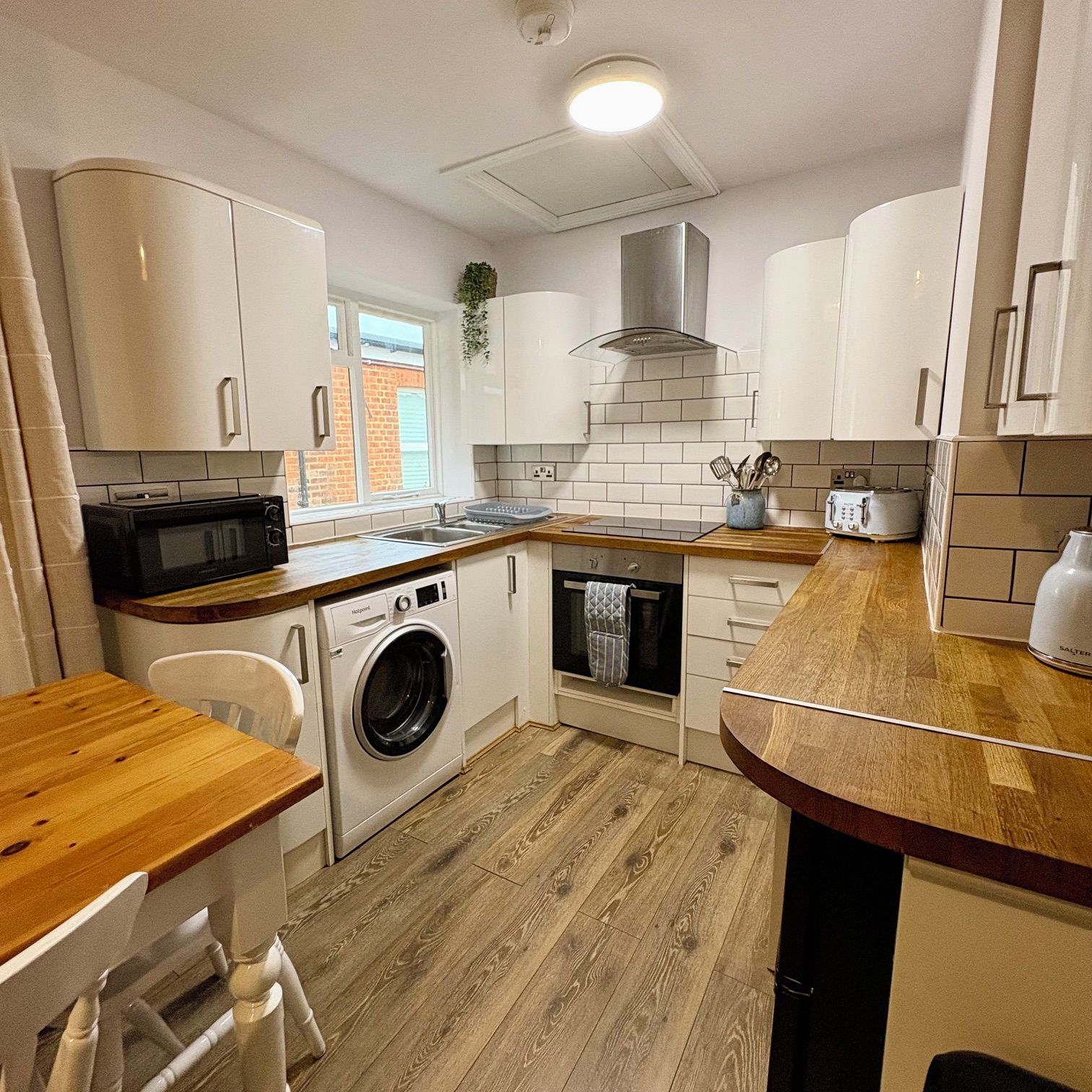 A compact kitchen with white cabinets, a microwave, a washing machine, and a toaster.
