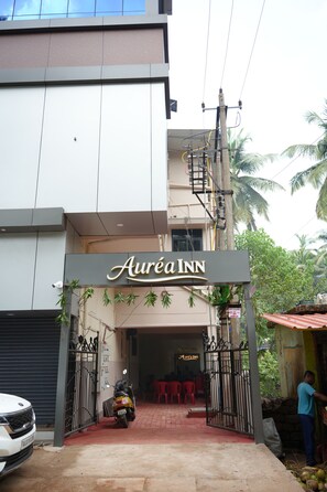 A hotel entrance with a sign reading 'Aurea Inn,' a gated driveway, a parked motorcycle, and a person standing by the entrance. - Aurea Inn (Gokarna)