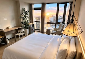 A hotel room with a large bed, a desk, a chair, a small table, and a potted plant. - SHANKEE Hotel Nguyen Thai Hoc (Ben Thanh)