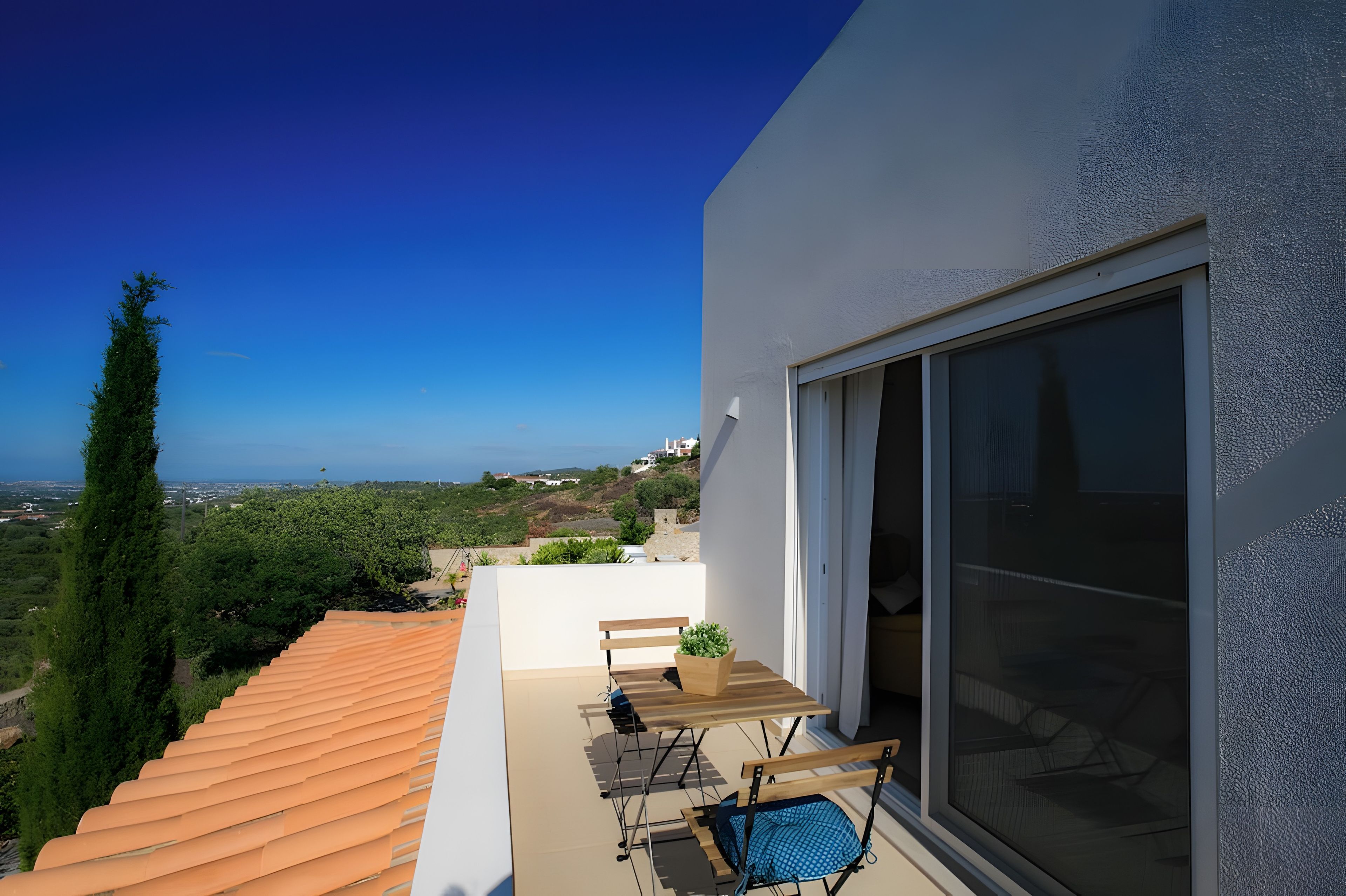 Un balcon avec vue sur la mer, un banc en bois et une table avec des chaises.