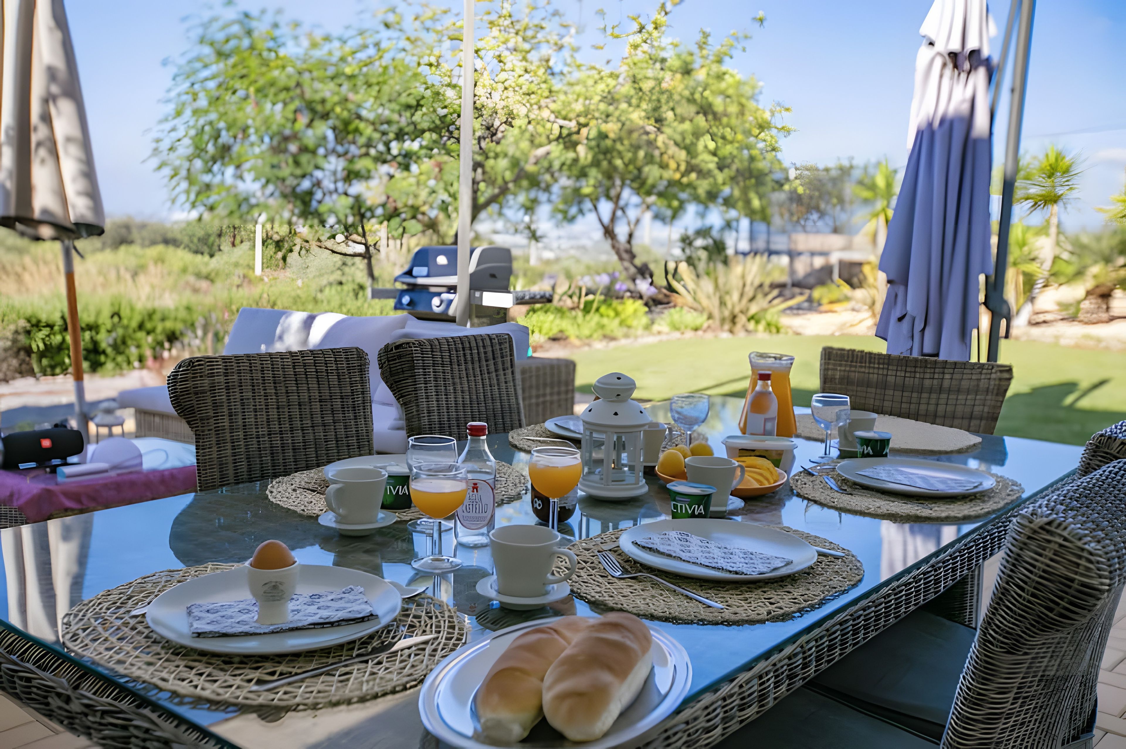 Un espace extérieur aménagé pour les repas, avec des meubles en osier, une table en verre et une vue sur le jardin.