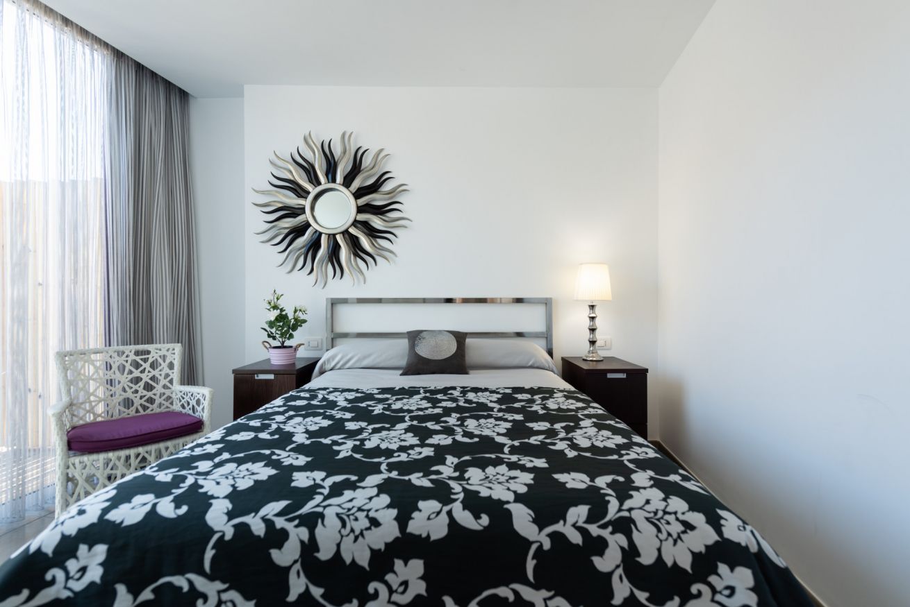 A hotel room with a bed, a nightstand, a lamp, a chair, and a decorative wall piece.