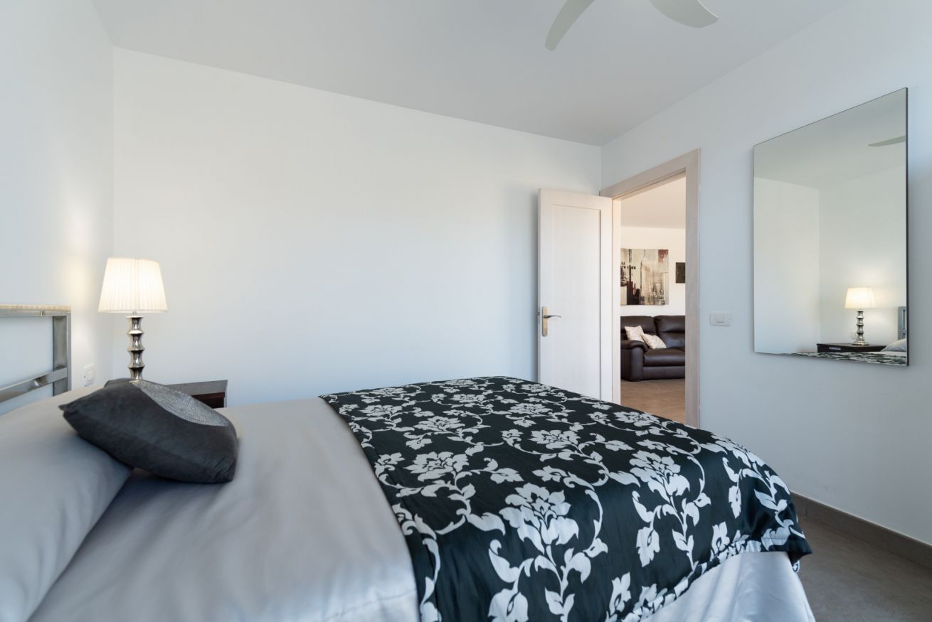 A hotel room with a bed, a bedside lamp, a door leading to a hallway, and a large mirror on the wall.