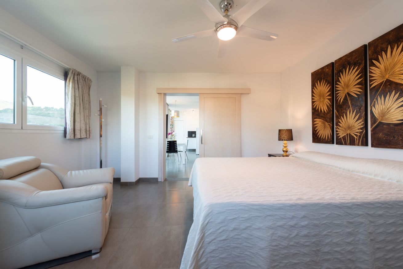 Un dormitorio con cama, una silla, ventilador de techo y cuadros en la pared.