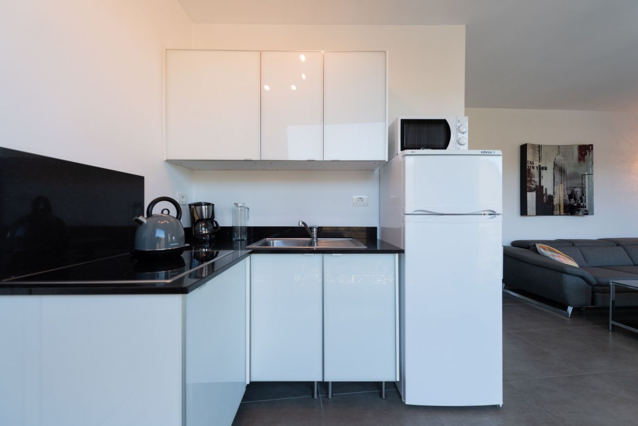 Una cucina moderna con mobili bianchi, un piano di lavoro nero, un bollitore, una macchina per il caffè e un frigorifero bianco.