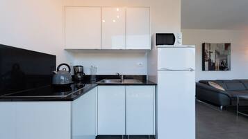 Una cucina moderna con mobili bianchi, un piano di lavoro nero, un bollitore, una macchina per il caffè e un frigorifero bianco.