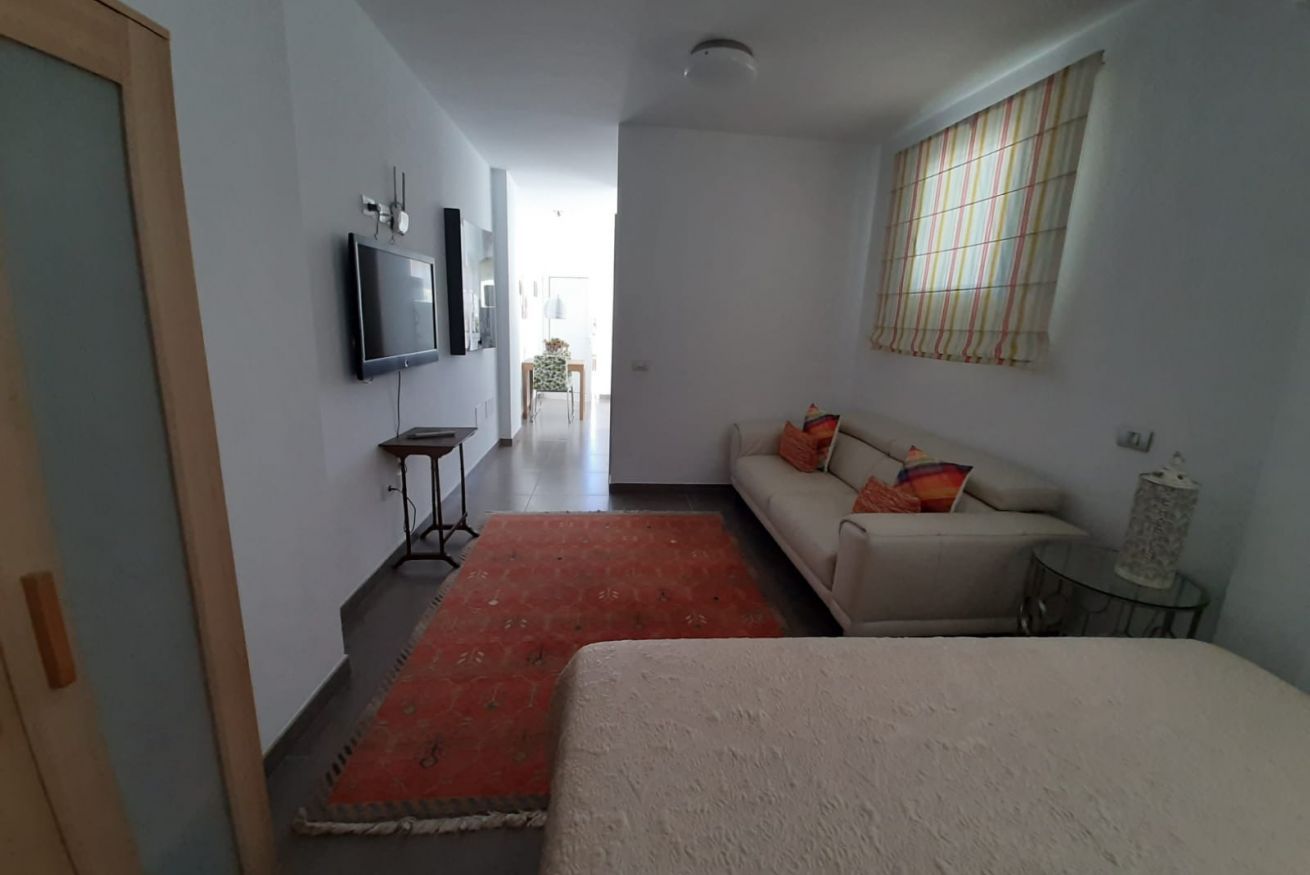 Una habitación con una cama, un sofá, un televisor en la pared y un ventanal con cortinas.