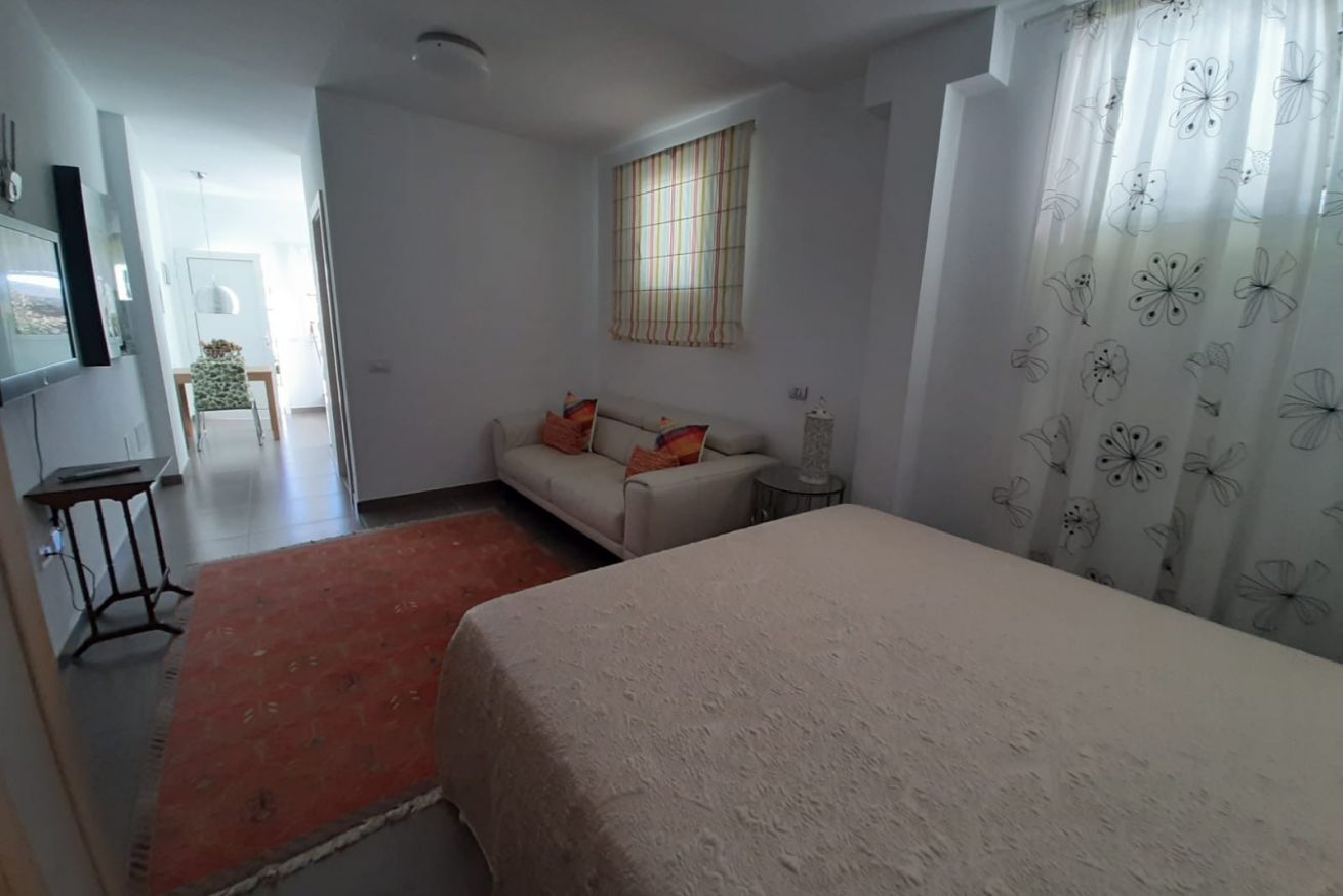 Une chambre à coucher avec un lit, un canapé, une petite table, une fenêtre avec des rideaux et un téléviseur fixé au mur.
