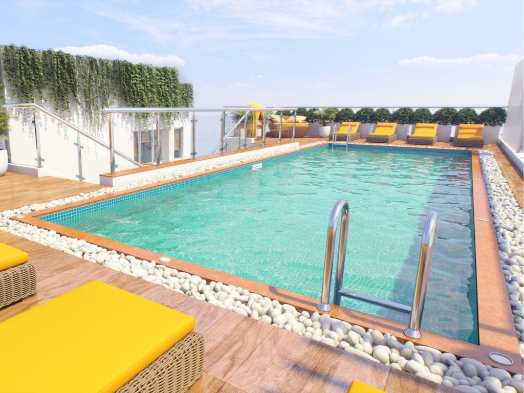 A rooftop pool with clear blue water, surrounded by white pebbles, yellow loungers, and a glass balustrade.