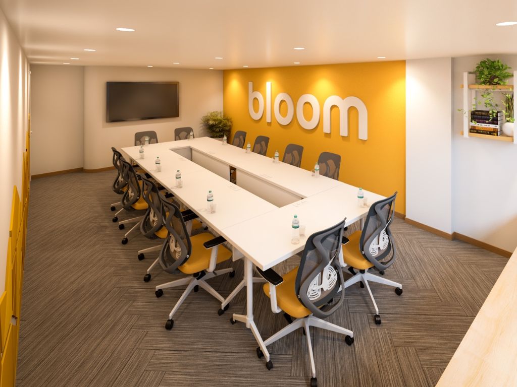 A conference room with a long table, chairs, and a 'bloom' sign on the wall.