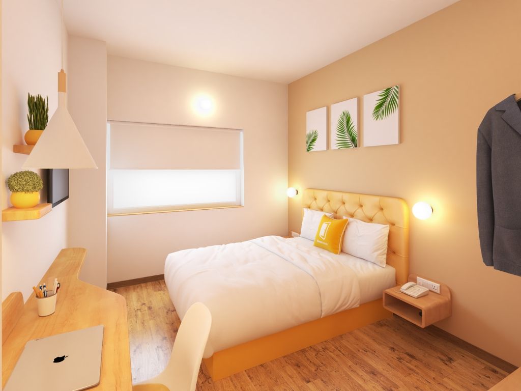 A modern bedroom with a bed, bedside table, lamp, and a desk with a laptop.