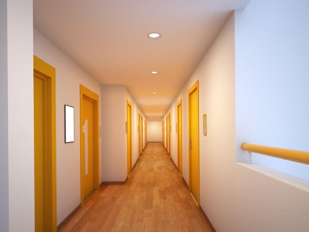 A long, narrow hallway with doors on both sides, wooden flooring, and a light-colored ceiling with recessed lighting.