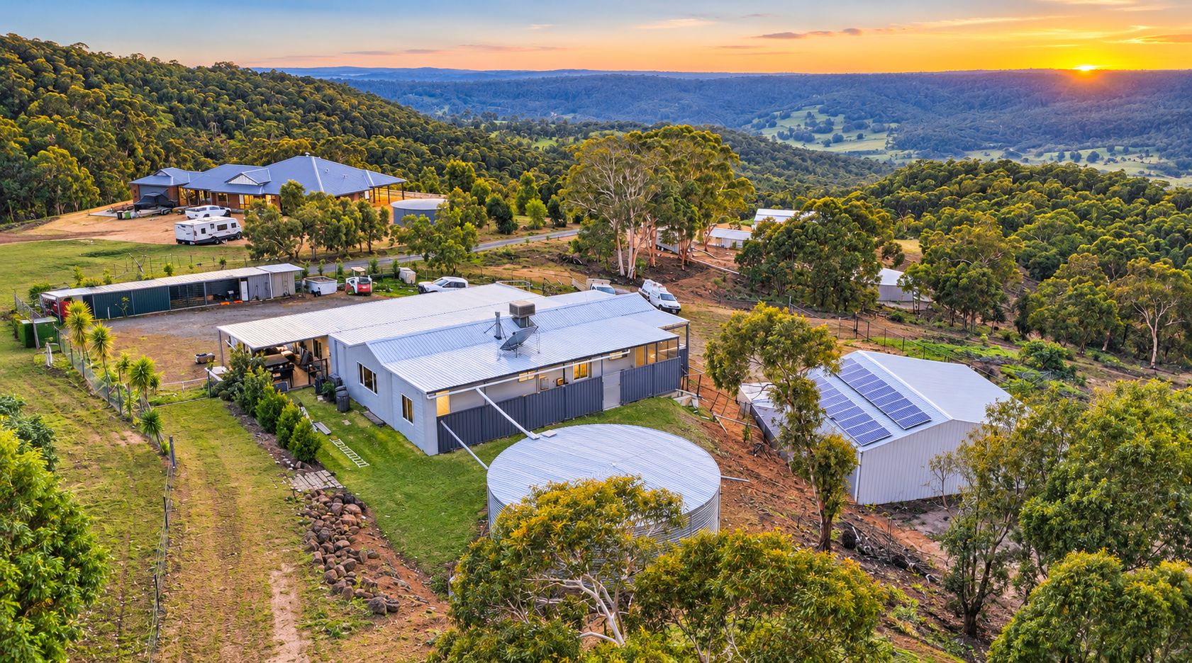 A residential area with multiple buildings, including a large house with a solar panel and a smaller structure.