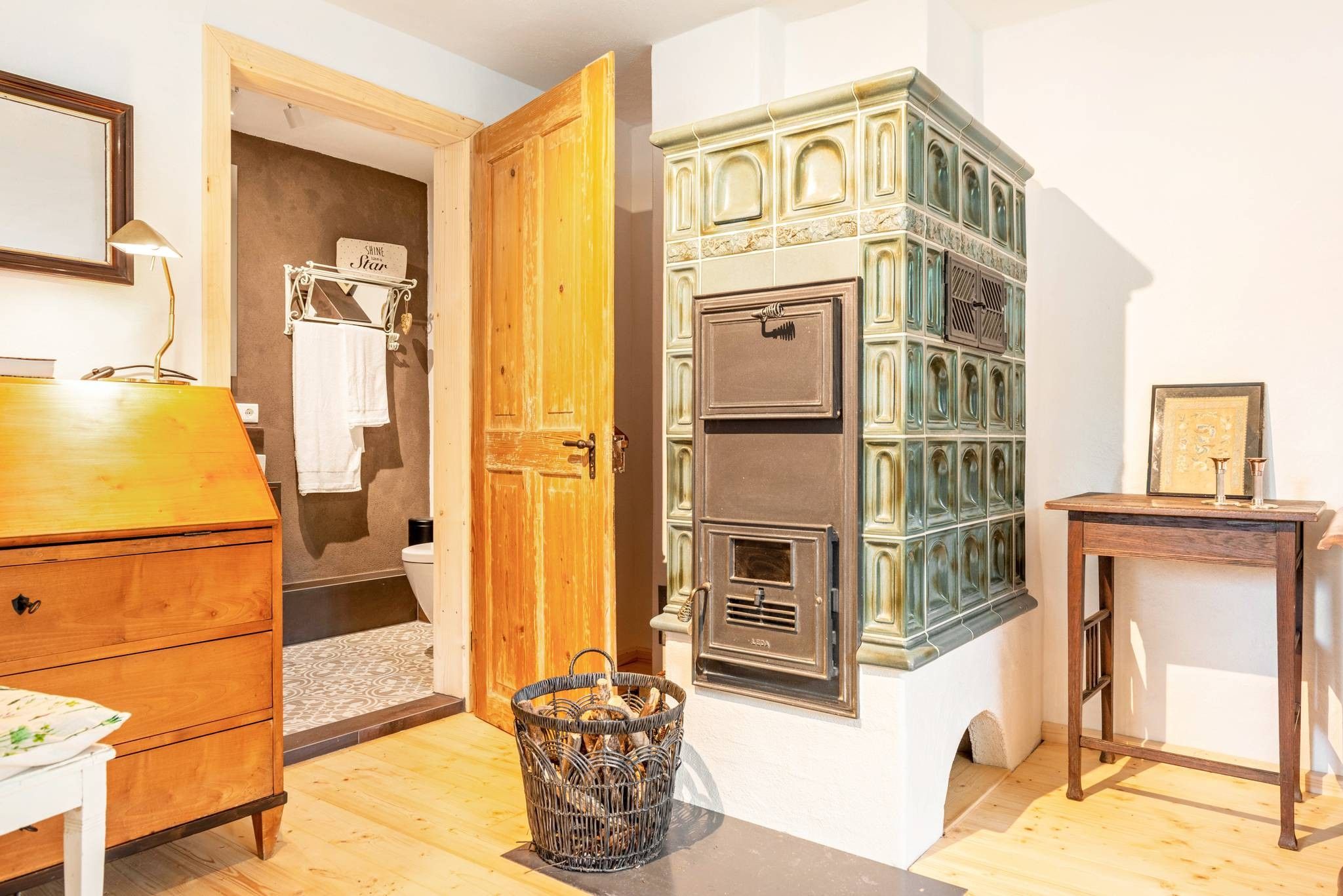 Ein Zimmer mit einem Holzkasten, einem Metallschrank, einem Korbwäschekorb und einem kleinen Tisch mit einer Lampe.