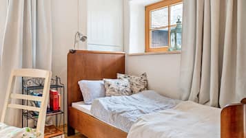 Ein Einzelbett mit Holz-Kopfteil, ein Nachttisch mit Lampe und ein Fenster mit Vorhängen.