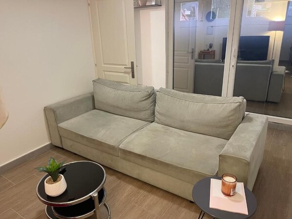 A modern living room with a grey sofa, a small round table with a plant, and a candle on a side table.