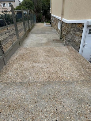 A gravel pathway leading to a building with a stone wall and a metal fence.