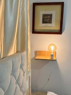 A room with a tufted headboard, a framed artwork on the wall, and a wall-mounted light fixture.