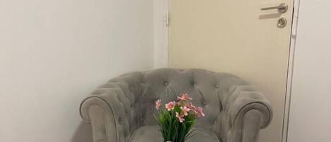 Ein Eckzimmer mit einem grauen, gesteppten Sofa und einem kleinen, runden Tisch mit einer Blumenvase.
