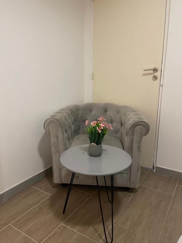 A corner room with a grey tufted sofa and a small round table with a vase of flowers.