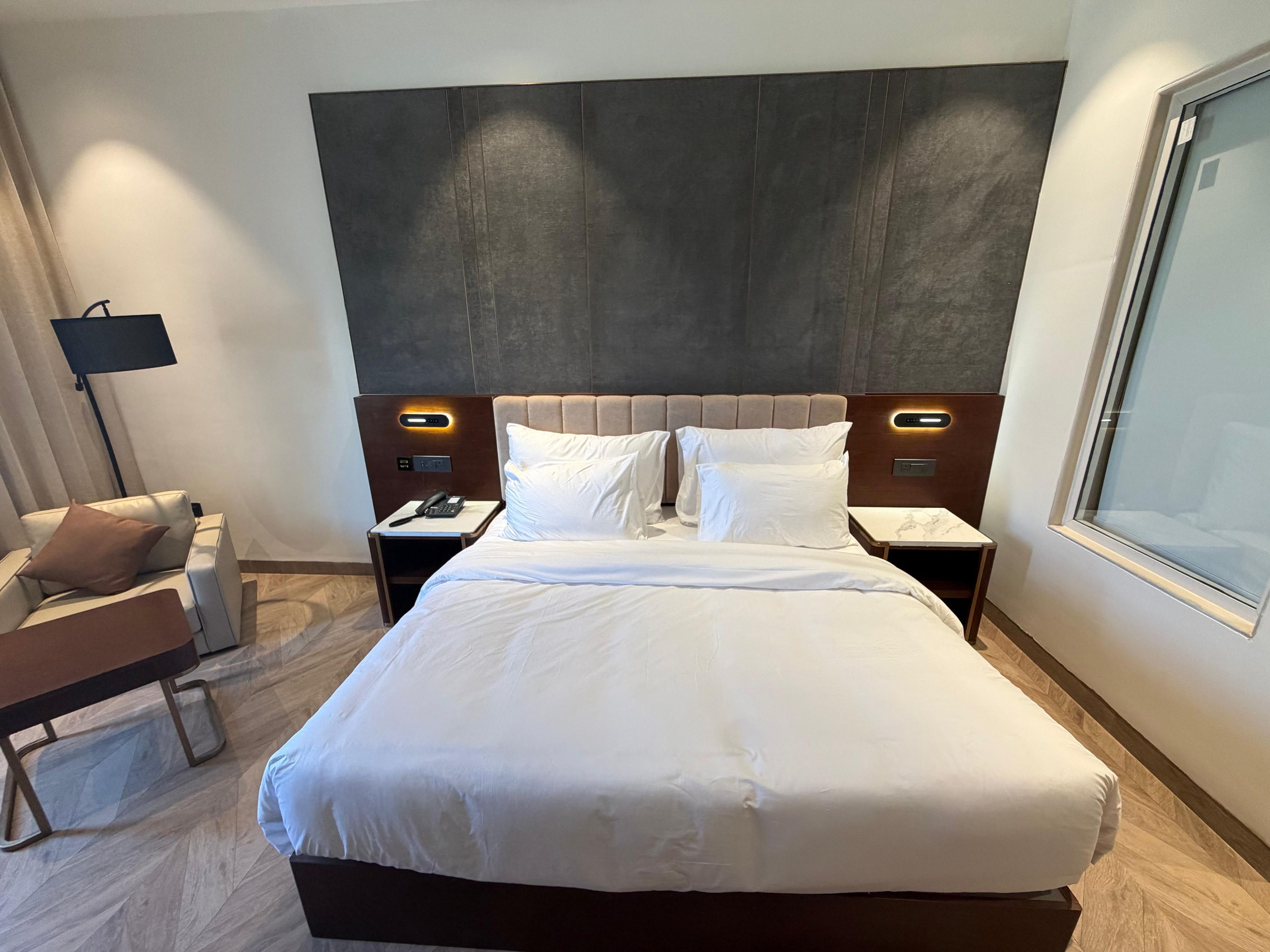 Habitación de hotel con una cama grande, una mesita de noche con teléfono, una lámpara y una silla.