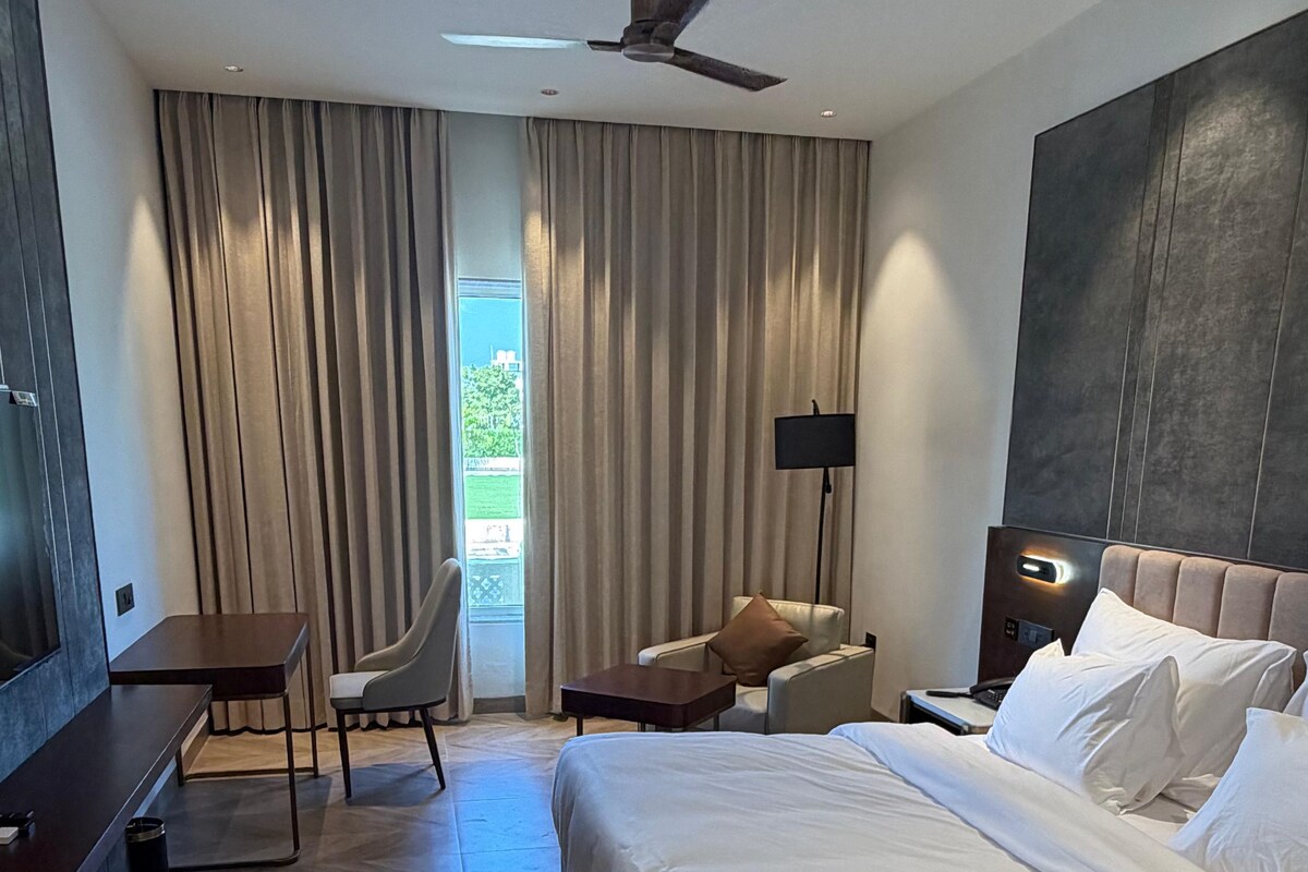 A hotel room with a bed, a desk, a chair, a TV, and a ceiling fan.