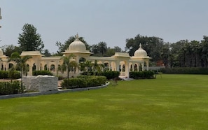 A large, open lawn area with a series of white domed structures and arches, surrounded by greenery and trees.