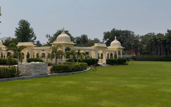 A large, open lawn area with a series of white domed structures and arches, surrounded by greenery and trees.