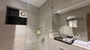 A modern bathroom with a glass shower enclosure, a built-in ventilation system, and a vanity with toiletries. - Sai Shree Hotel (Shirdi)