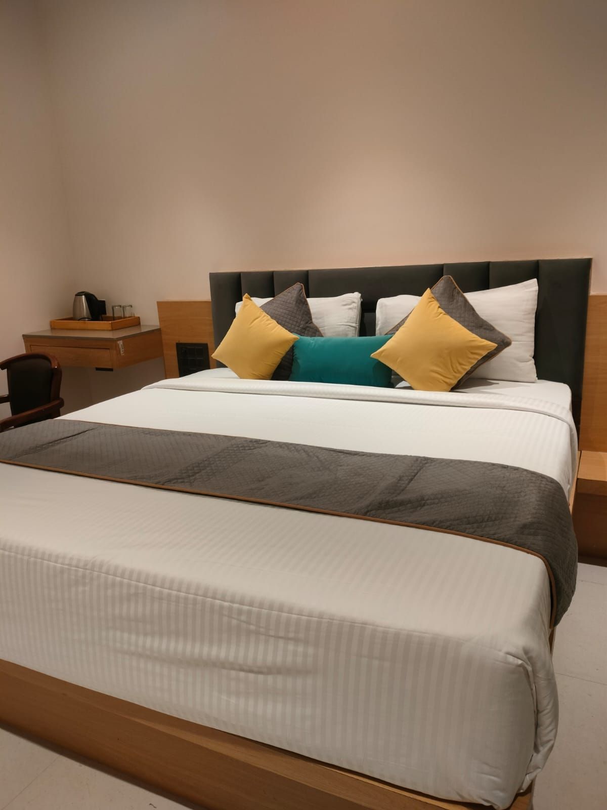 Una cama con cabecera, una mesita de noche con hervidor y una bandeja.