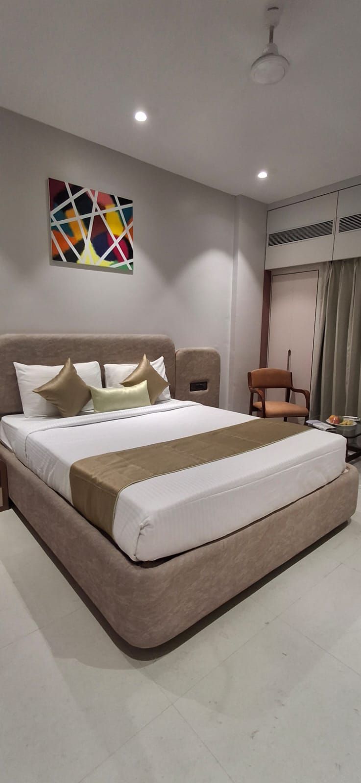 Una camera da letto con un letto grande, una sedia, un tavolino e un quadro astratto dai colori vivaci appeso al muro.