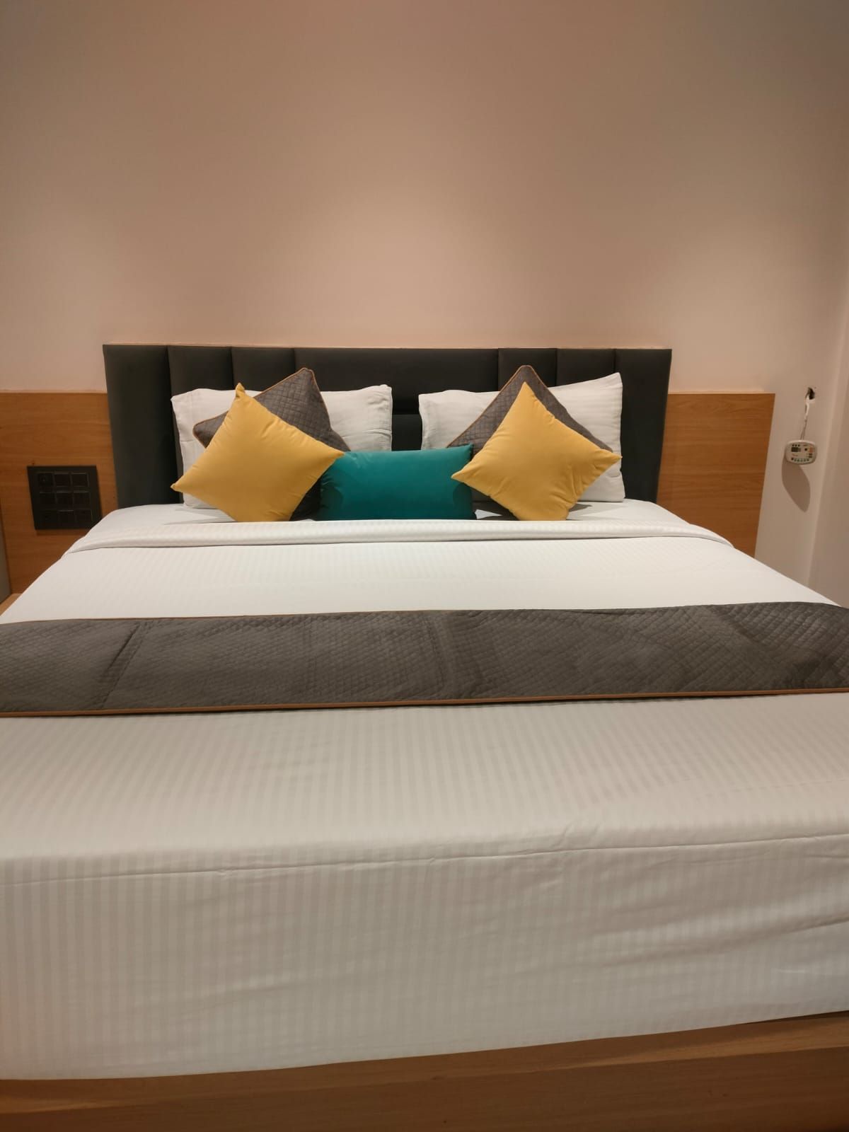 En pænt redt seng med gavl, et natbord og en stikkontakt på væggen.