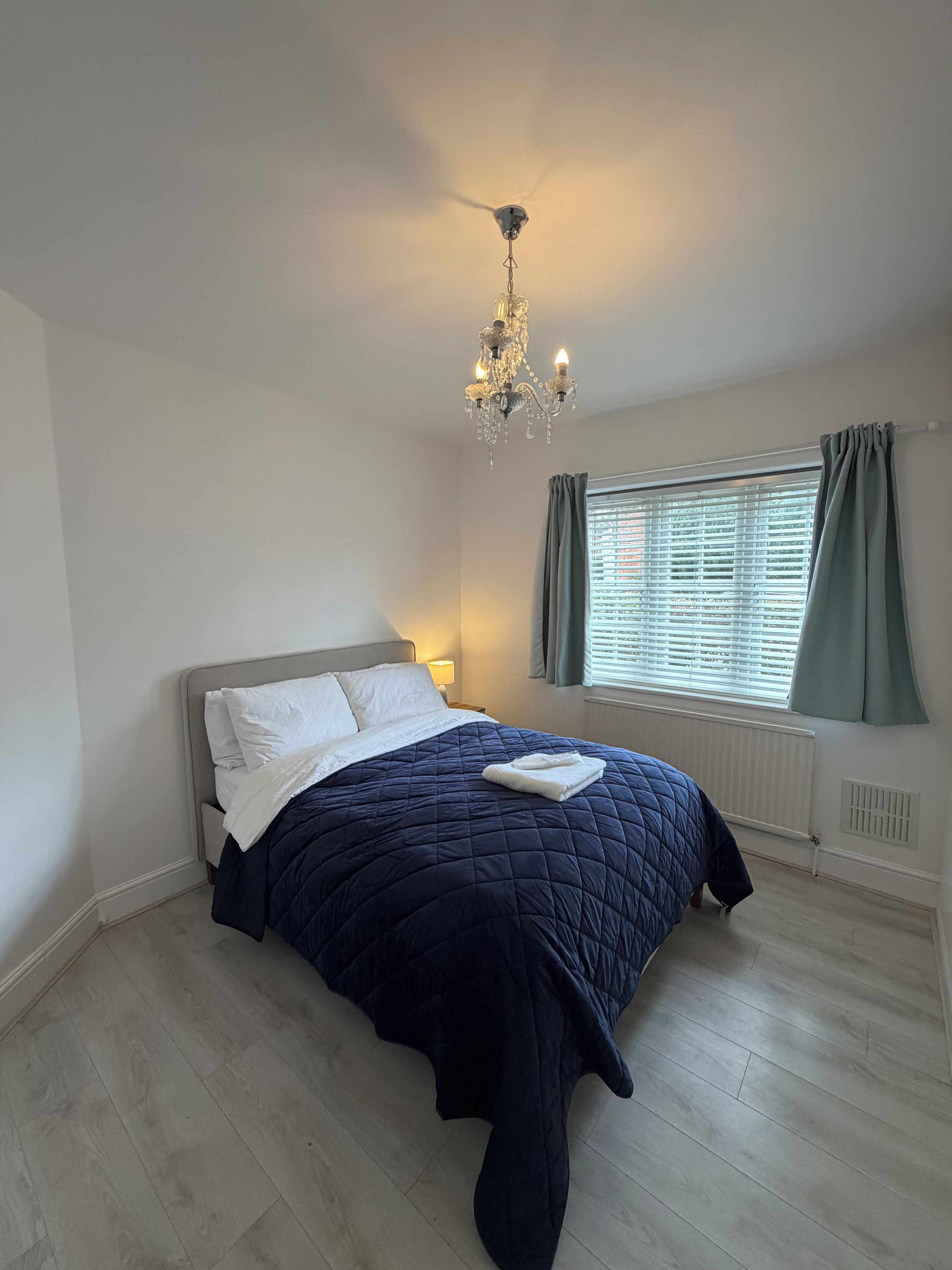 A bedroom with a bed, a chandelier, a window with curtains, and a radiator.