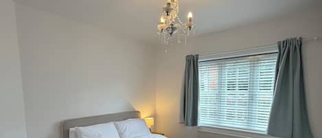 Une chambre à coucher avec un lit, un lustre, une fenêtre avec des rideaux et un radiateur.