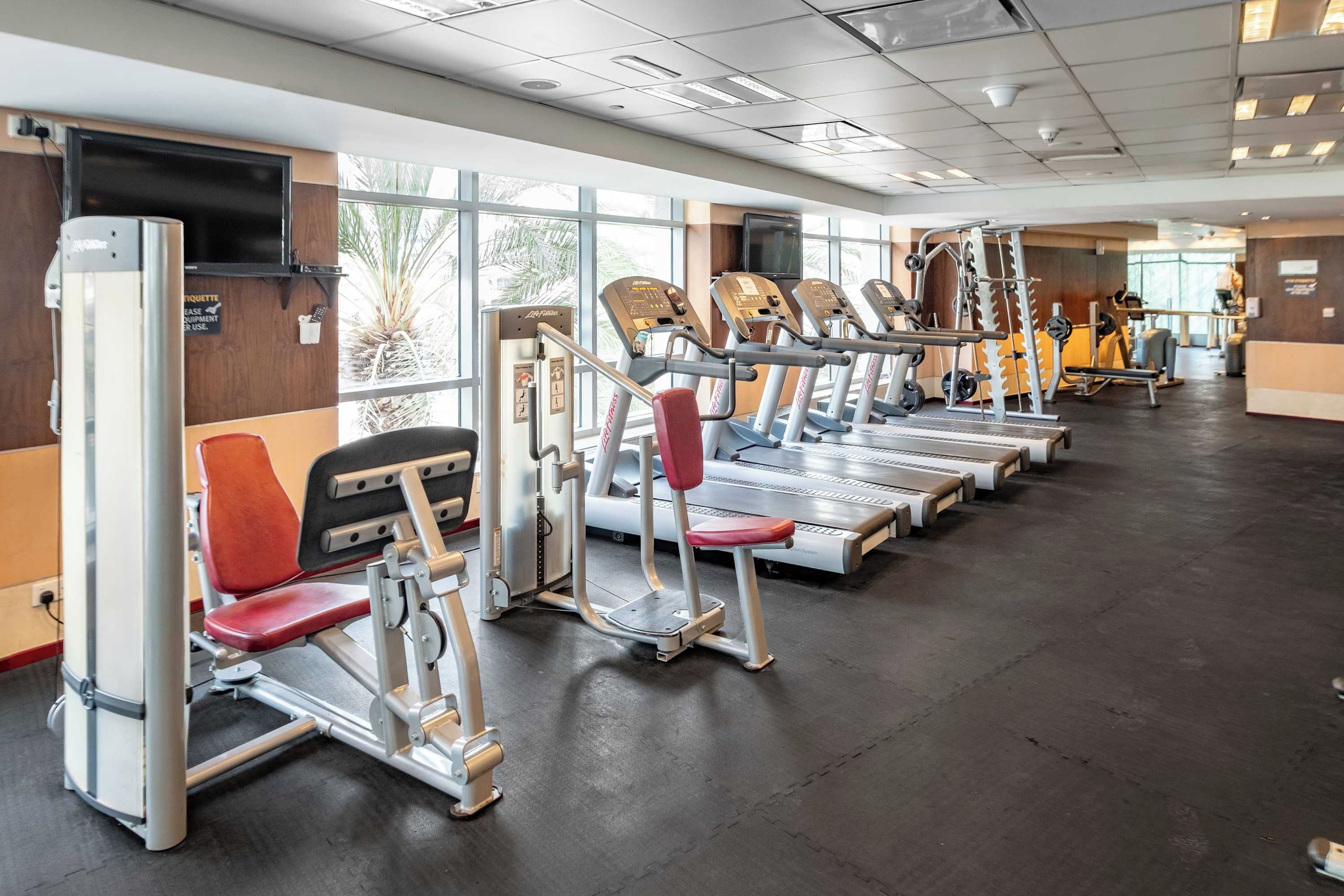 Une salle de sport équipée de plusieurs tapis de course, de machines de musculation et d’une grande fenêtre laissant entrer la lumière naturelle.