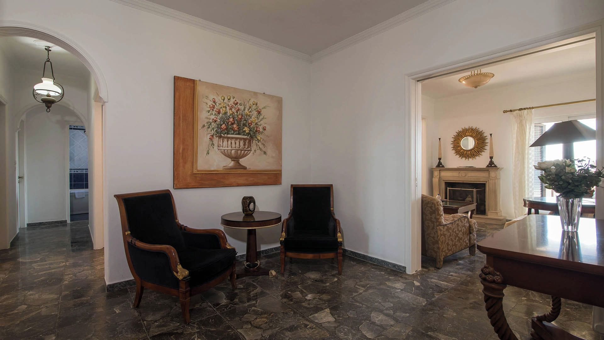 Een kamer met een open haard, een eettafel, twee fauteuils, een klein rond tafeltje en een schilderij aan de muur.