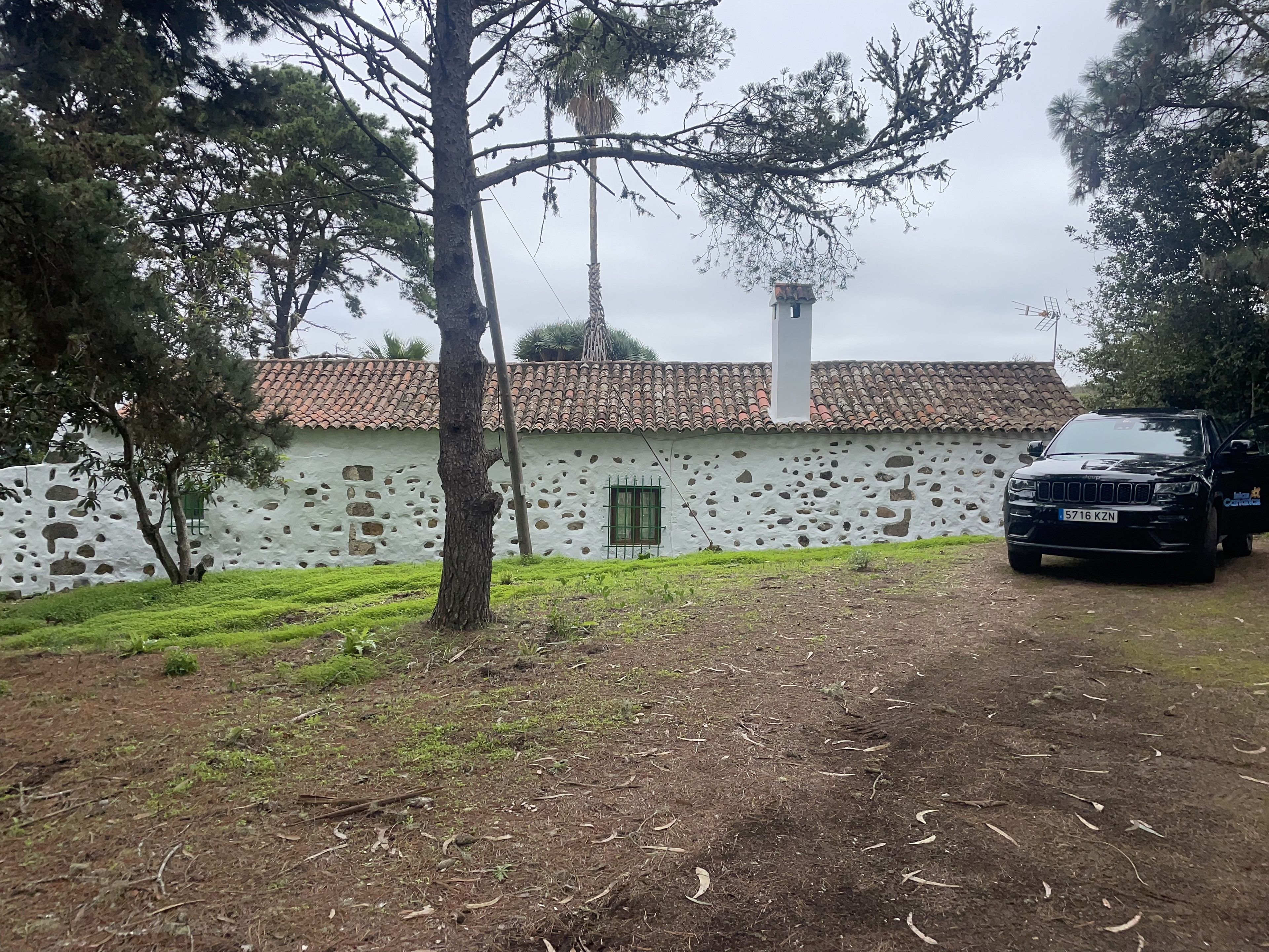 A rustic building with a stone facade, a tiled roof, and a parked black vehicle.