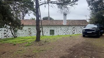 A rustic building with a stone facade, a tiled roof, and a parked black vehicle.