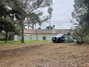 Una casa con pared de piedra y techo de tejas, rodeada de árboles y un coche estacionado.