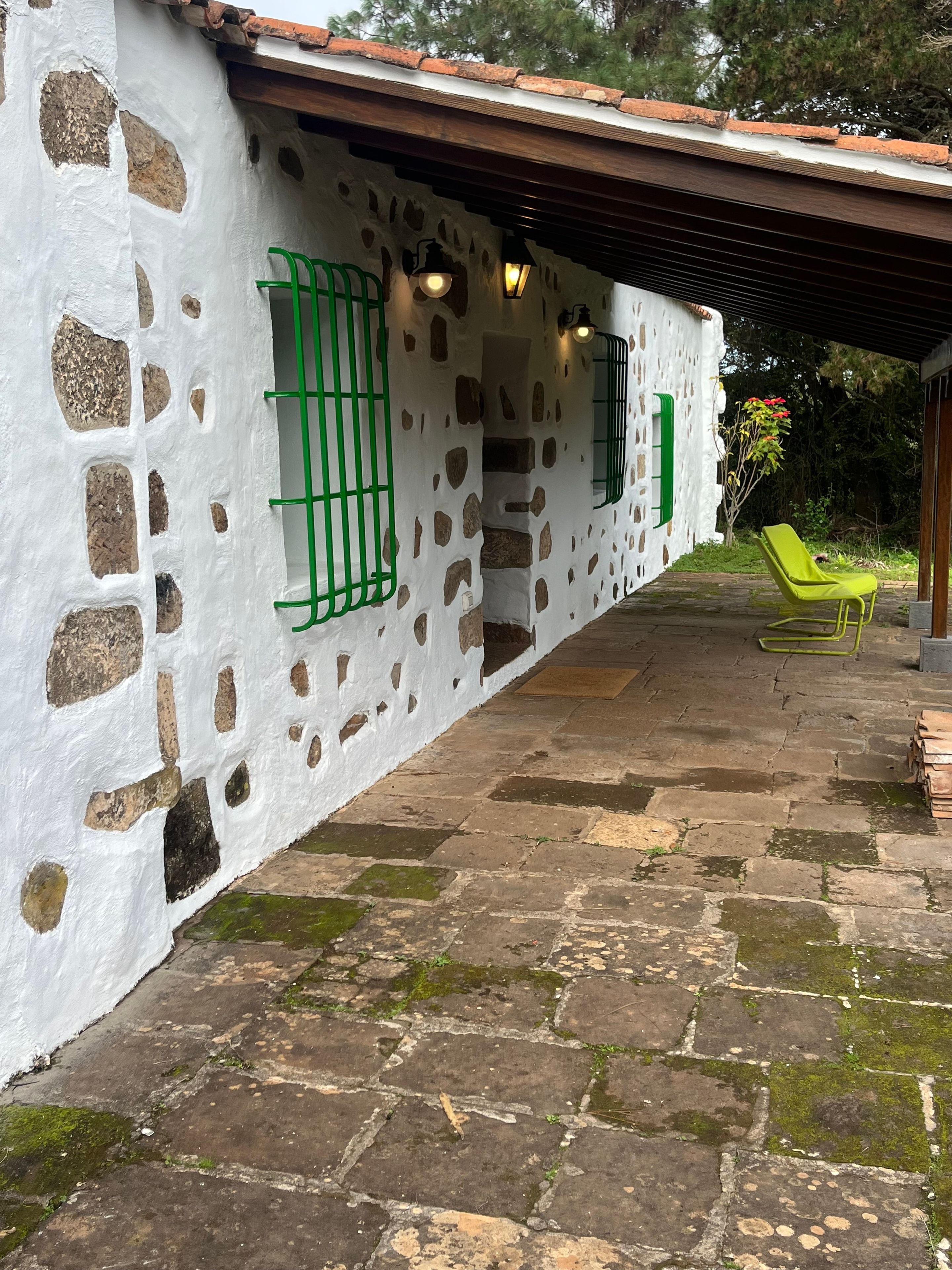 A stone-paved patio with a white wall featuring irregular stone patterns and green window bars.