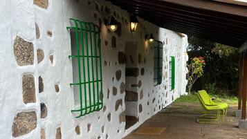 A stone-paved patio with a white wall featuring irregular stone patterns and green window bars.