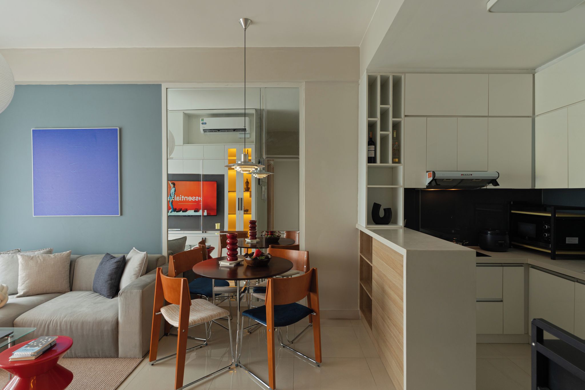 A modern living room with a sofa, dining table, and chairs. There is a kitchen area with cabinets and appliances.