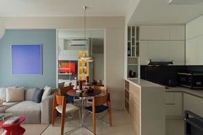 A modern living room with a sofa, dining table, and chairs. There is a kitchen area with cabinets and appliances. - Kaleido Home 2BR 75m2 Landmark 81 View, Bathtub, The Sun Avenue, Pool & Gym (Thành phố Hồ Chí Minh)