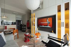 A modern living room with a flat-screen TV, a glass coffee table, and a red accent chair. - Kaleido Home 2BR 75m2 Landmark 81 View, Bathtub, The Sun Avenue, Pool & Gym (Thành phố Hồ Chí Minh)