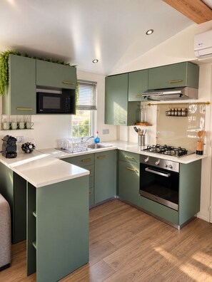 A modern kitchen with green cabinets, a microwave, stove, oven, and a window with blinds. - New Listing (Vias)