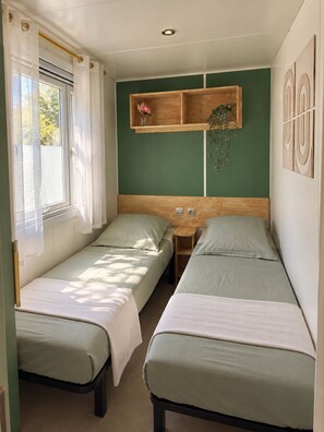 Une chambre avec deux lits simples, une tête de lit en bois, une table de chevet et une étagère murale agrémentée d’un vase et d’une plante.