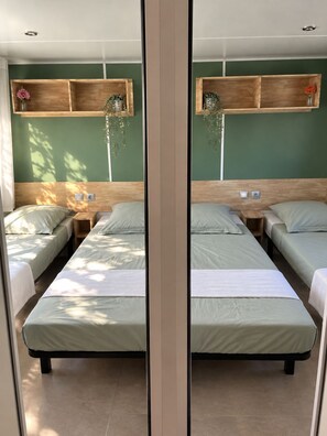 A mirrored view of a hotel room with two beds, a wooden headboard, a shelf with plants, and a window allowing natural light. - New Listing (Vias)