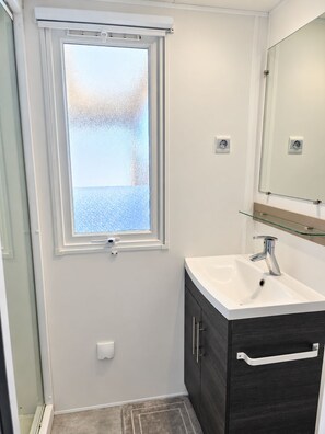 A bathroom with a window, a sink, a mirror, and a dark cabinet. - New Listing (Vias)